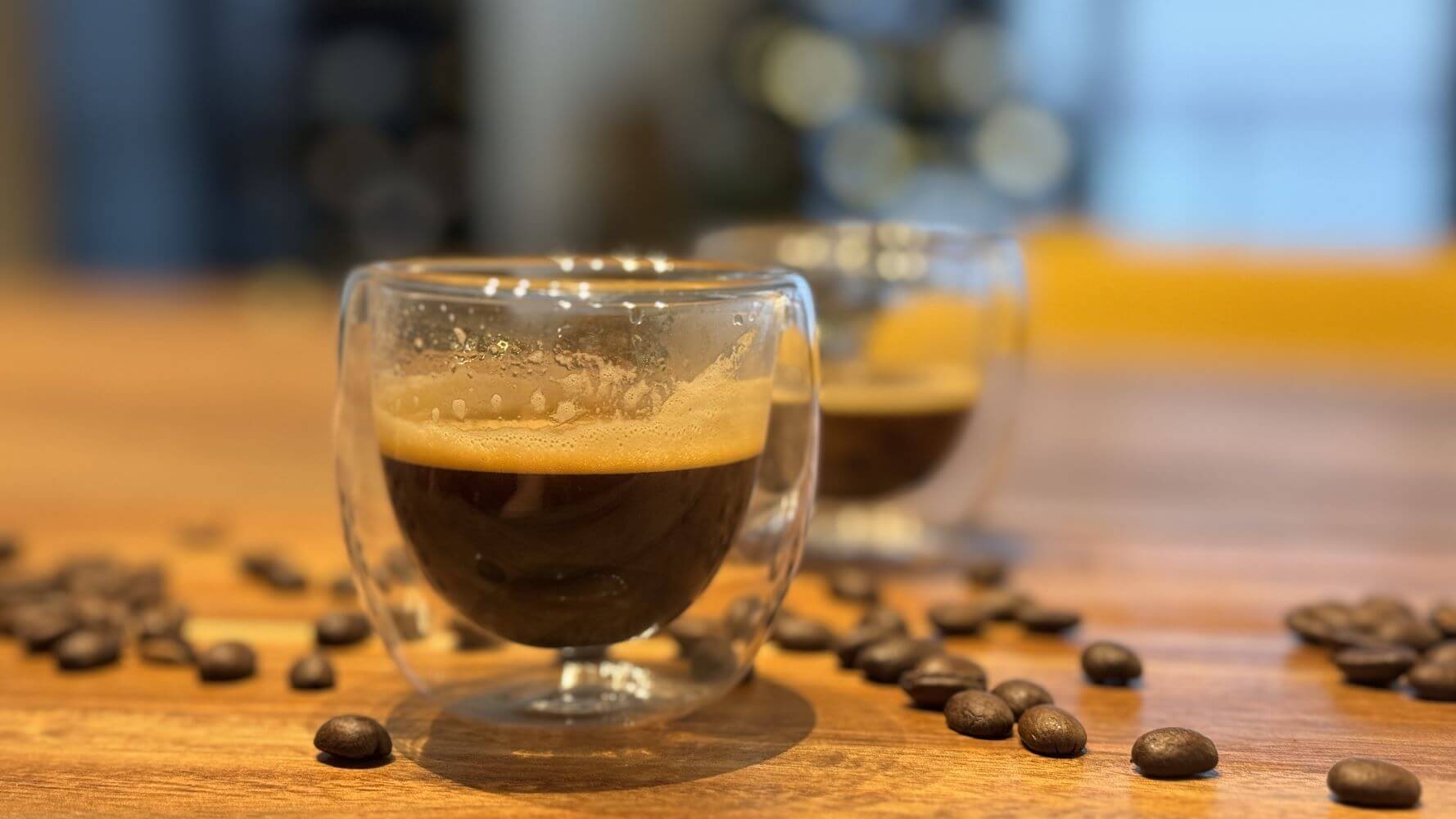 Tasse à café double paroi en gros plan posée sur une planche en bois avec des grains de cafés torréfiés autour.