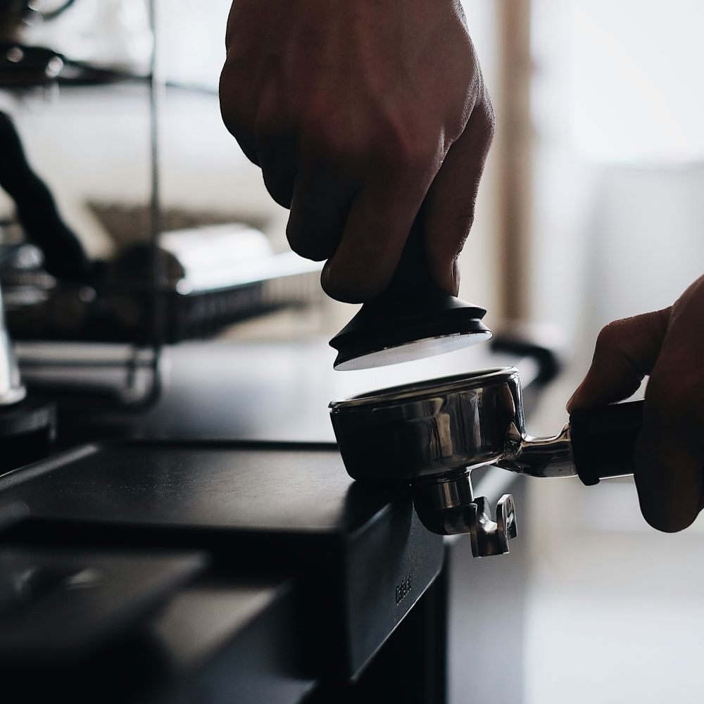 Barista qui utilise un tamper sur un tapis de tassage pour répartir la mouture de café dans un porte filtre.