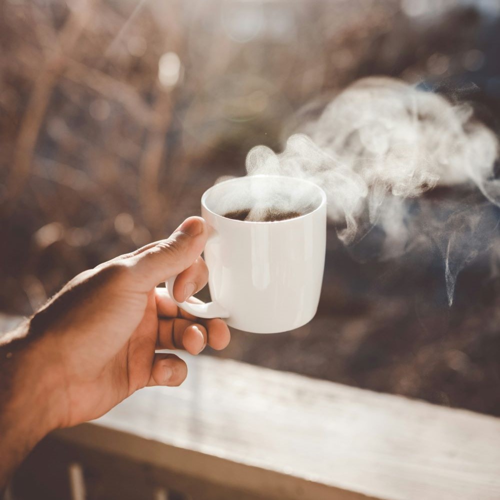 Café du matin dans une grande tasse qui fume près d'une fenêtre.