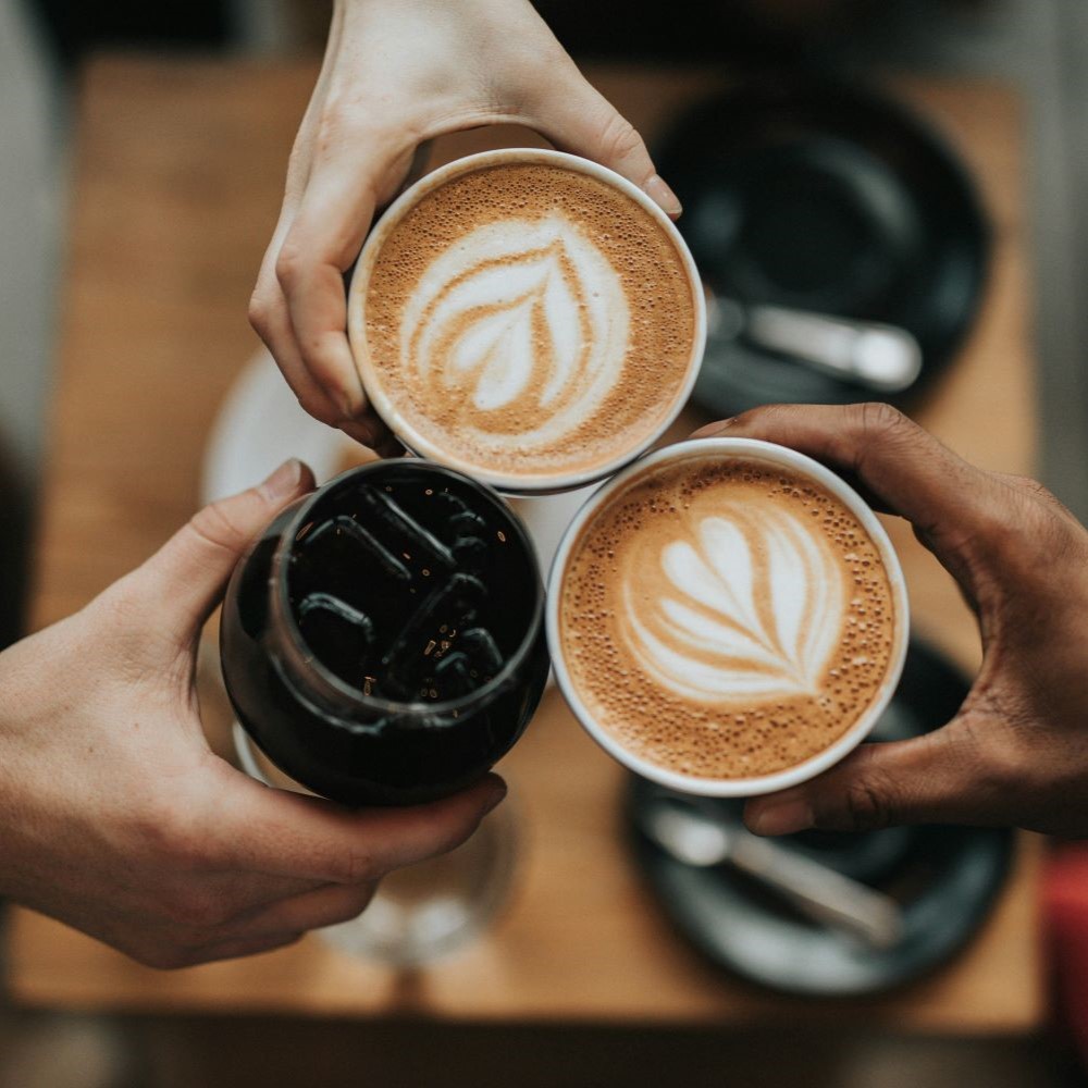 Trois amis qui trinquent des tasses avec différents types de cafés.