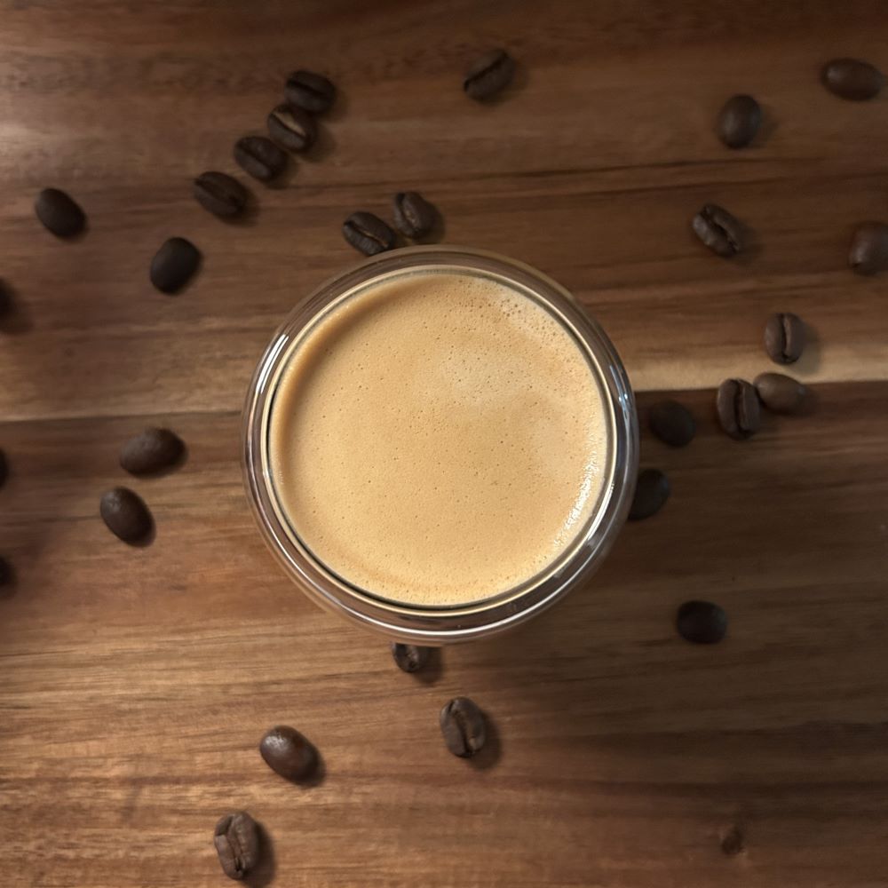 Planche en bois avec une tasse de café double paroi vue de haut remplie d'un expresso avec des grains de café autour.