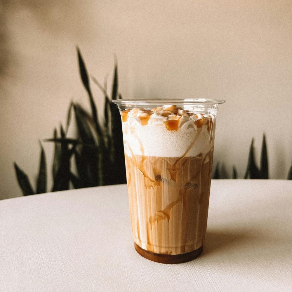 Verre posé sur une table avec un café glacé au caramel et une belle mousse de lait par-dessus.