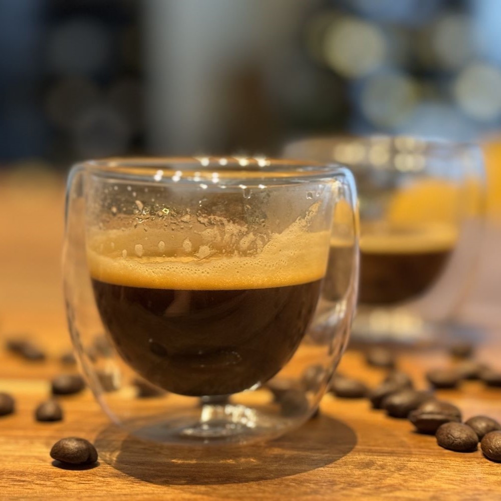 Tasse à café double paroi en gros plan posée sur une planche en bois avec des grains de cafés torréfiés autour.