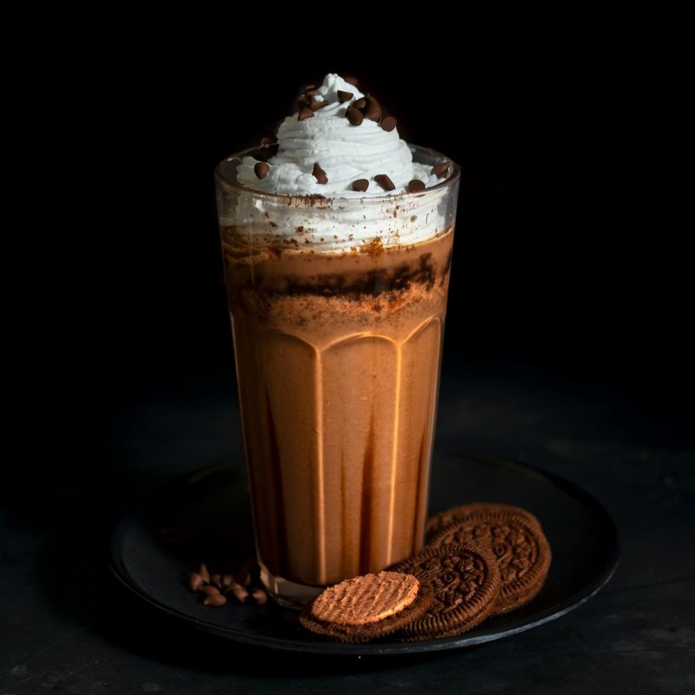 Smoothie au café et au chocolat servi avec de la chantilly et des pépites de chocolat par-dessus dans un verre transparent.