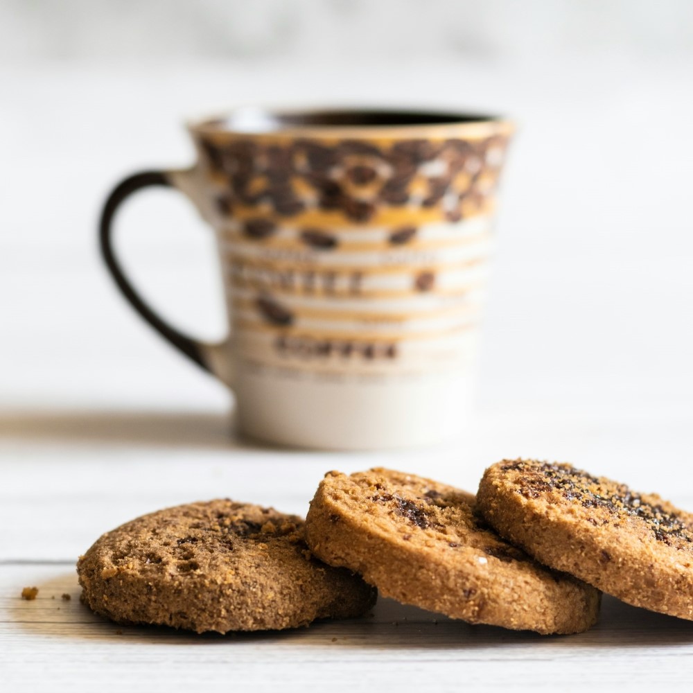 Trois cookies au chocolat posés devant une tasse de café